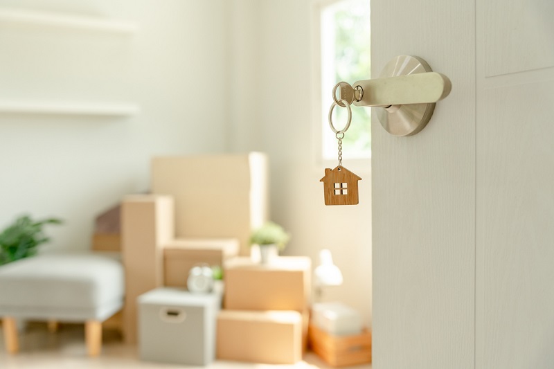 A door ajar, with a key in it, showing moving boxes inside.