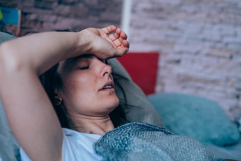 Woman woken up at night from night sweats. Has her hand on her forehead to feel the warmth.