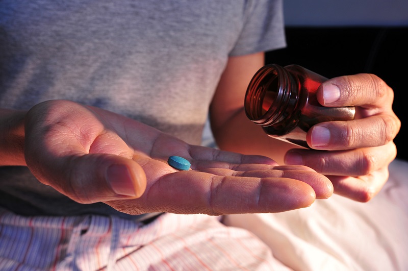 Man's hands pouring out a blue pill for erectile dysfunction.